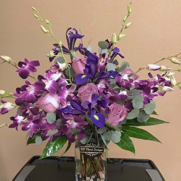 Purple orchids and pink roses arranged in a clear glass vase