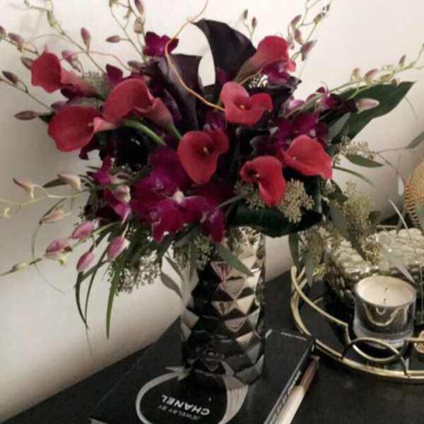 Tall bouquet of red calla lilies and purple orchids in a patterned vase