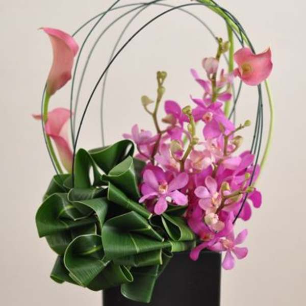 Pink calla lilies and orchids in a black vase with arched stems