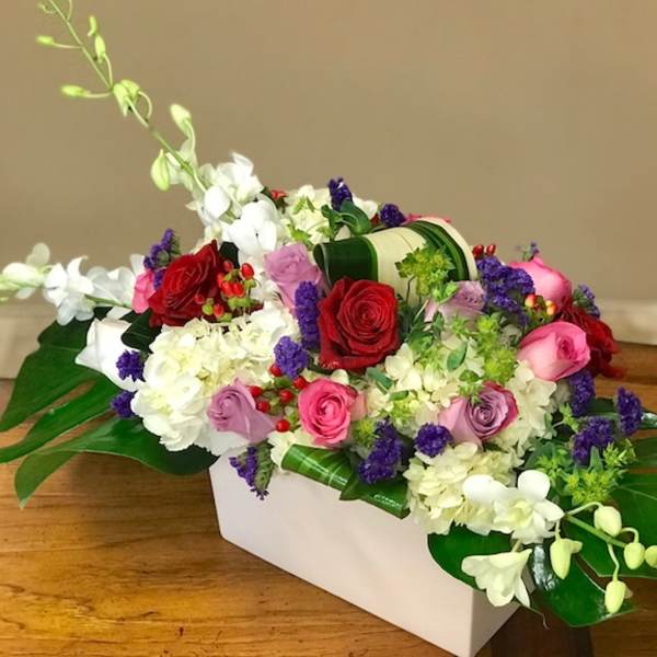 Mixed roses and orchids arranged in a white rectangular vase