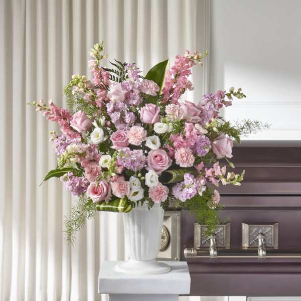 Pink and white floral spray in a white urn beside a casket