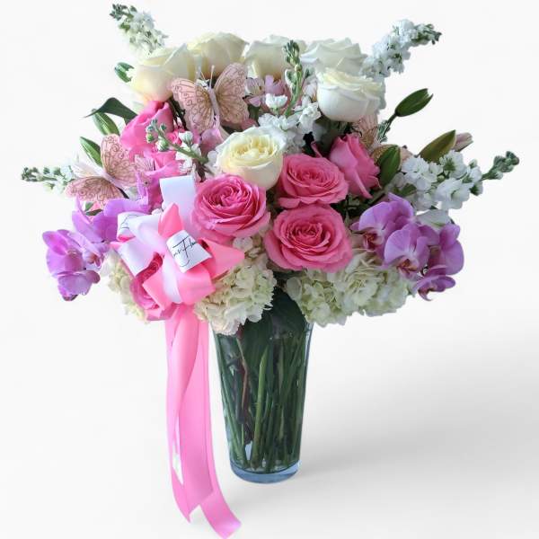 Tall glass vase of pink and white roses, orchids, and hydrangeas with pink ribbon and butterfly accents