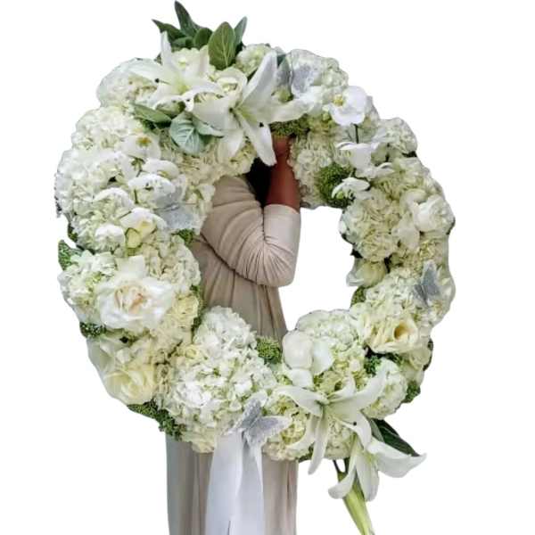 Large white floral wreath with lilies and hydrangeas held by a person