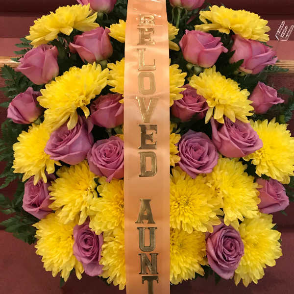 Pink roses and yellow chrysanthemums with a vertical ribbon reading "BELOVED AUNT"
