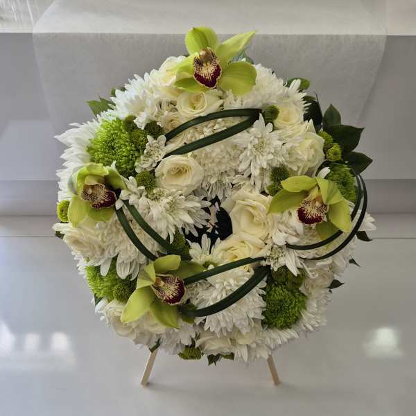 Round white floral arrangement with green orchids and roses on a stand