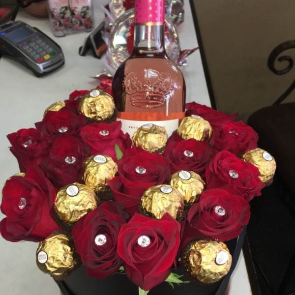 Red roses and gold-wrapped chocolates arranged around a wine bottle in a black box