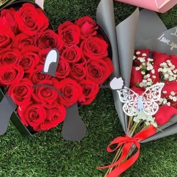 Heart-shaped box of red roses beside a wrapped bouquet of red roses