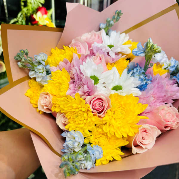 Bouquet of pink roses, yellow chrysanthemums, and white daisies in pink wrap