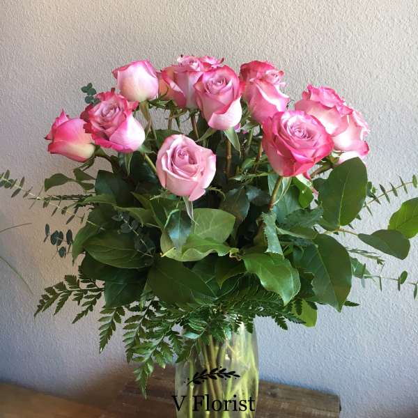 Tall arrangement of pink roses in a clear glass vase on a wooden surface