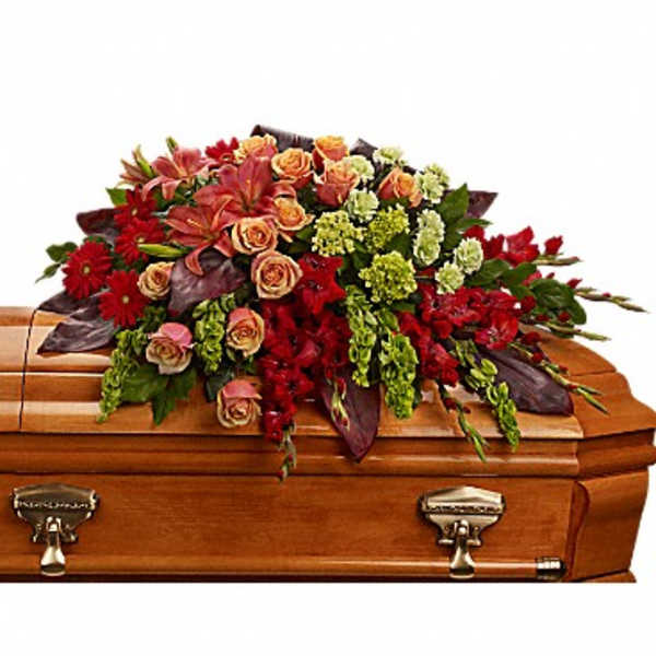 Casket spray with red and peach flowers on a wooden casket