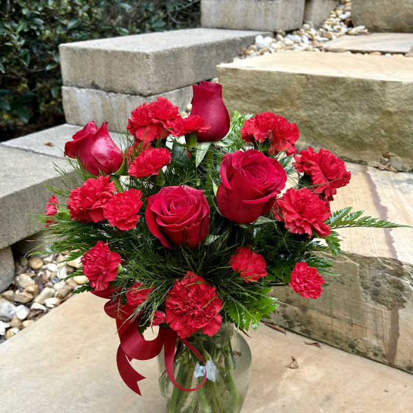 Red roses and carnations arranged in a clear glass vase with a red ribbon.