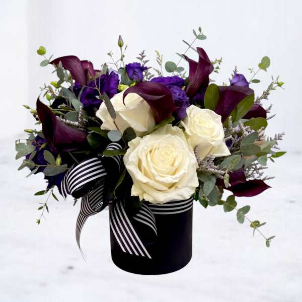 Bouquet of white roses, purple flowers, and dark calla lilies in a black vase