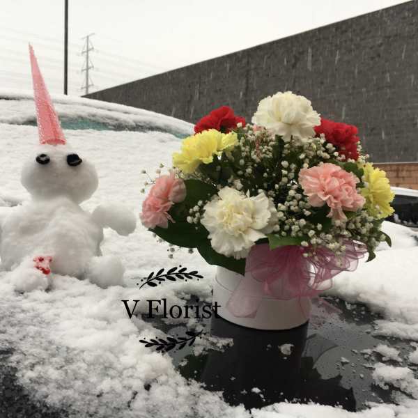 Round white box of mixed carnations with baby’s breath in snow beside a small snow figure.