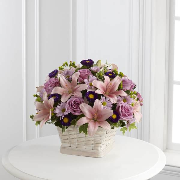 Pink lilies, roses, and purple daisies in a white basket