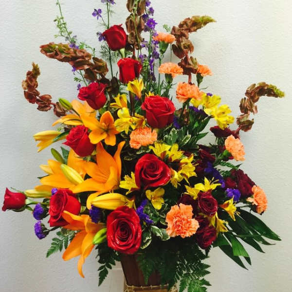 Tall mixed arrangement of red roses, orange lilies, and assorted blooms in a wooden container