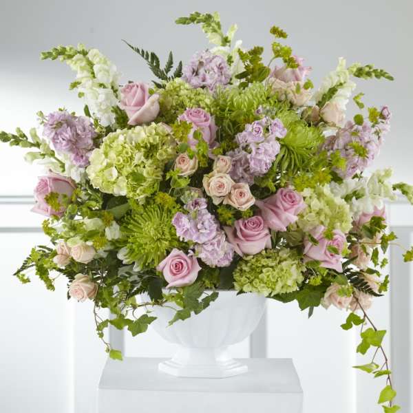 Large pastel floral arrangement in a white urn vase