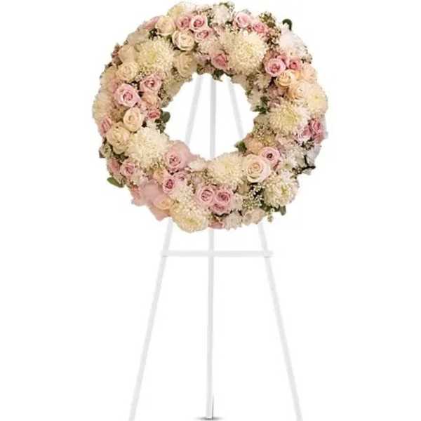 Round floral wreath of pale pink and cream flowers on a white stand