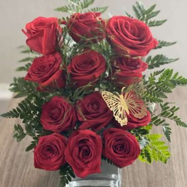 Red roses arranged in a clear square vase with fern accents