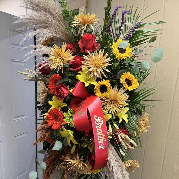 Tall standing floral spray with red and yellow flowers and a red ribbon