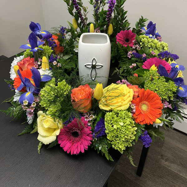 Colorful floral wreath around a white urn with a cross emblem
