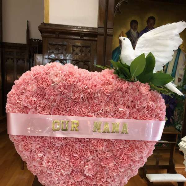 Pink carnation heart arrangement with a white dove topper and ribbon