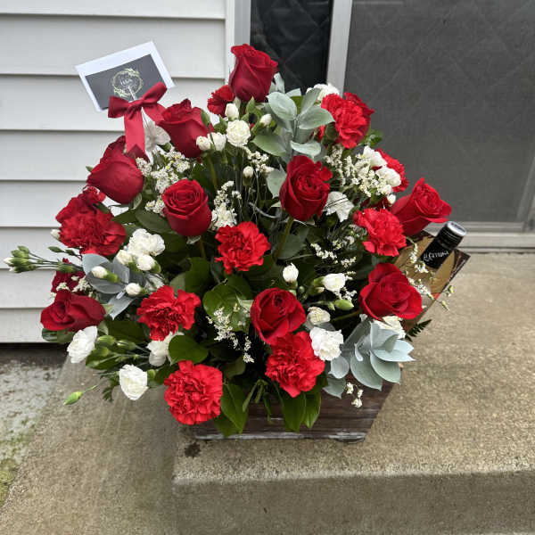Red roses and carnations in a wooden basket with a ribbon and card.