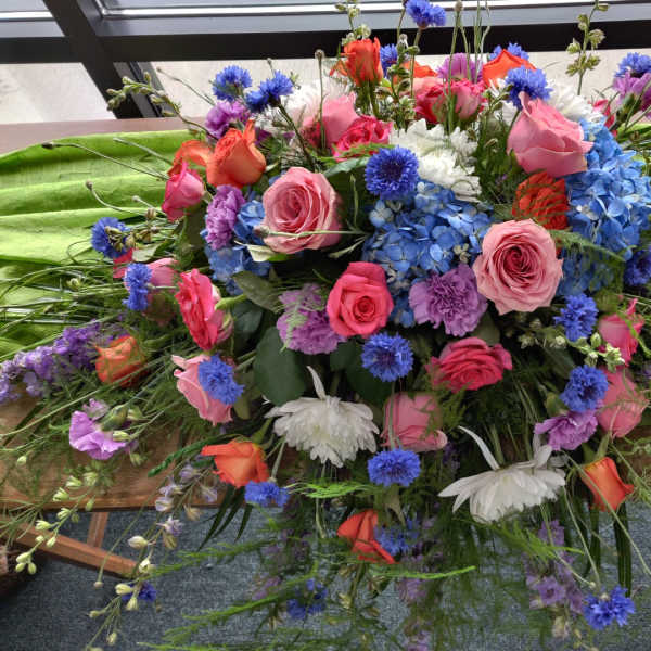 Colorful floral casket spray with roses, hydrangeas, and daisies