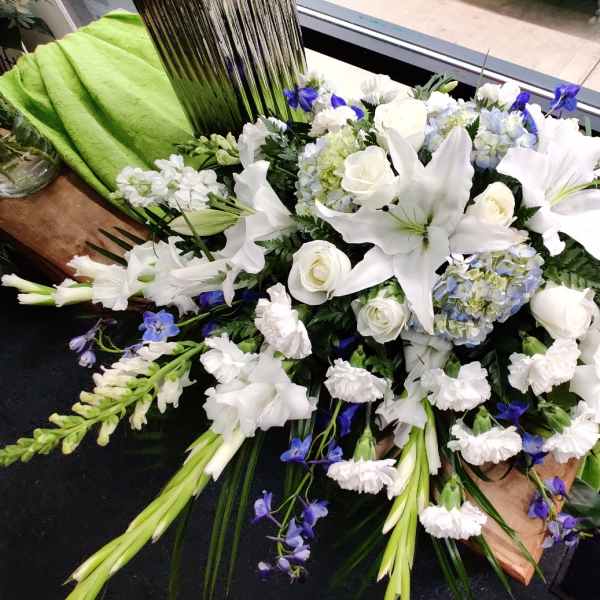White lilies and roses with blue accents in a large casket spray