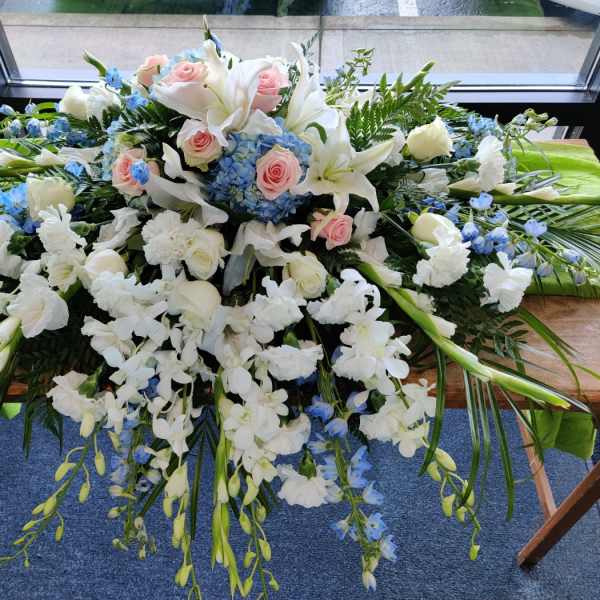 Large white floral casket spray with pink roses and blue accents