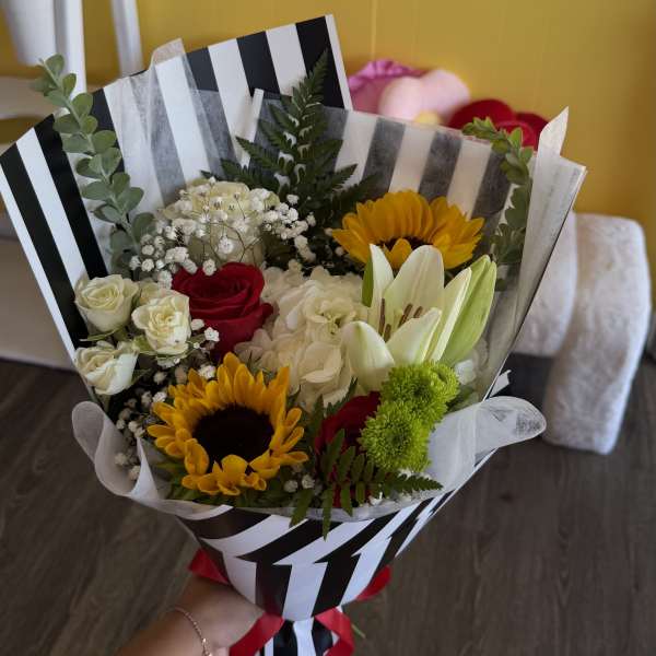 Bouquet of sunflowers, roses, lilies, and hydrangea wrapped in striped paper