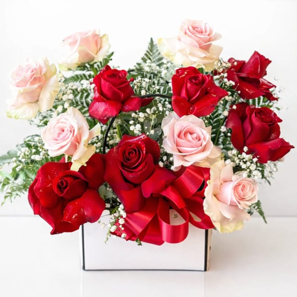 Red and blush roses arranged in a white box with a red ribbon