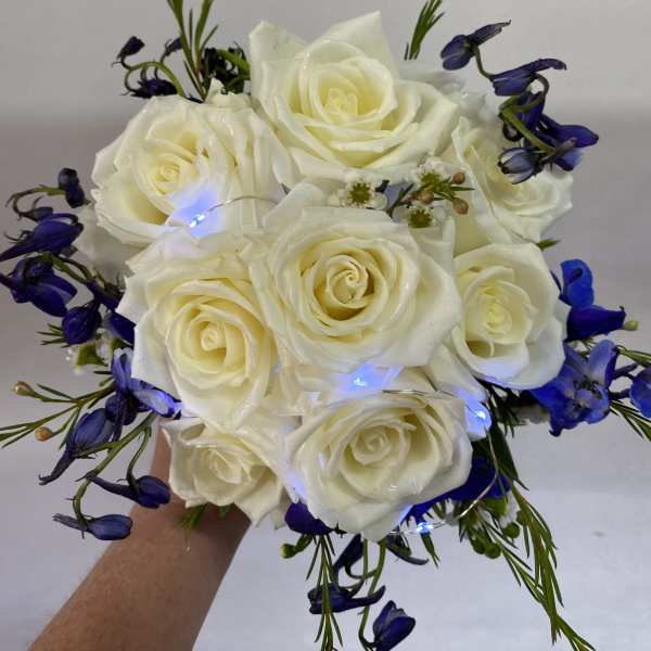Handheld bouquet of white roses with blue flowers and small lights