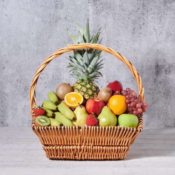Wicker basket filled with assorted fruit including pineapple, grapes, apples, pears, bananas, and kiwi