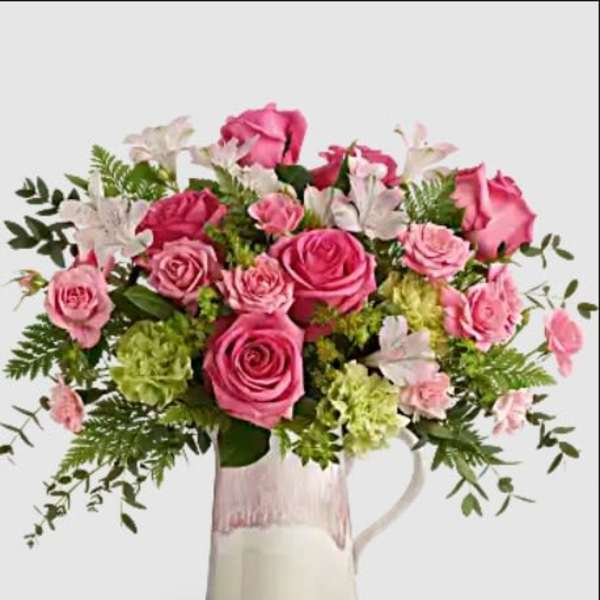 Pink roses and white flowers arranged in a glass pitcher vase