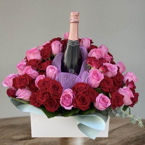 Pink and red roses arranged around a champagne bottle in a white box