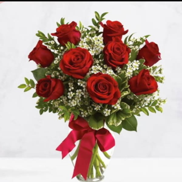 Bouquet of red roses with white filler flowers in a glass vase and pink ribbon