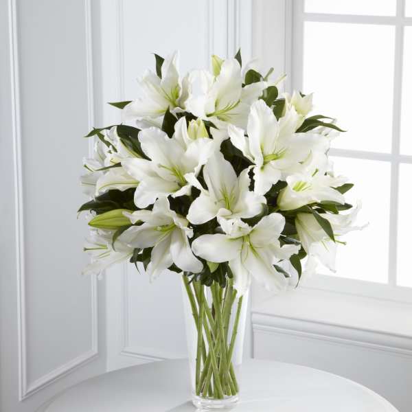 Tall clear vase filled with large white lilies on a round white table