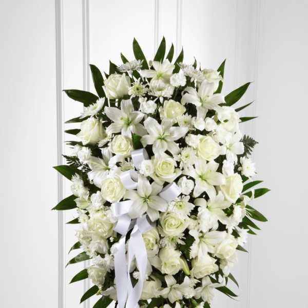 Oval white standing spray with lilies, roses, and carnations on an easel stand.