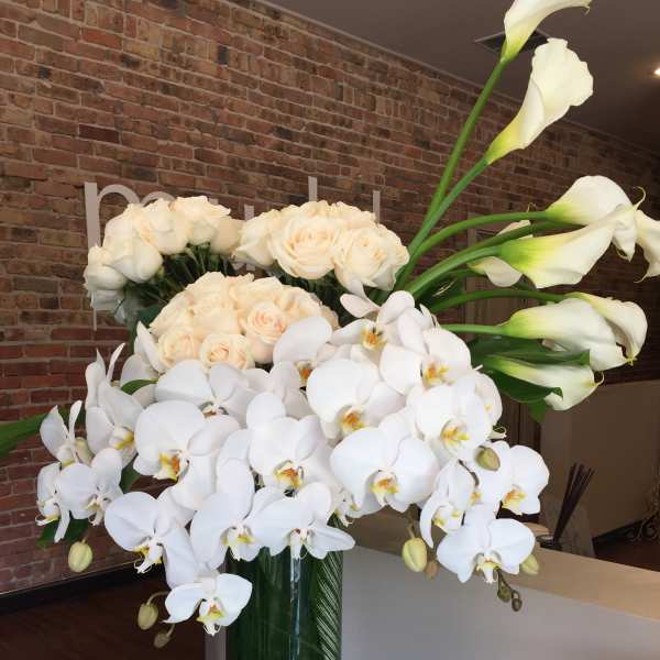 White orchids, roses, and calla lilies in a tall glass vase