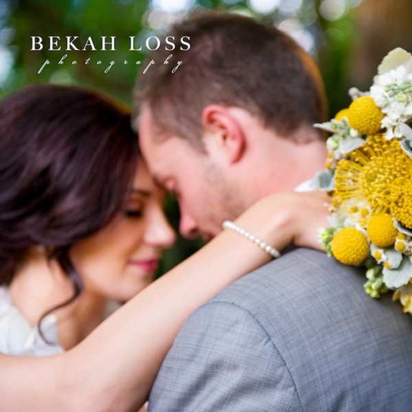 Bride and groom embracing beside a yellow and white bouquet