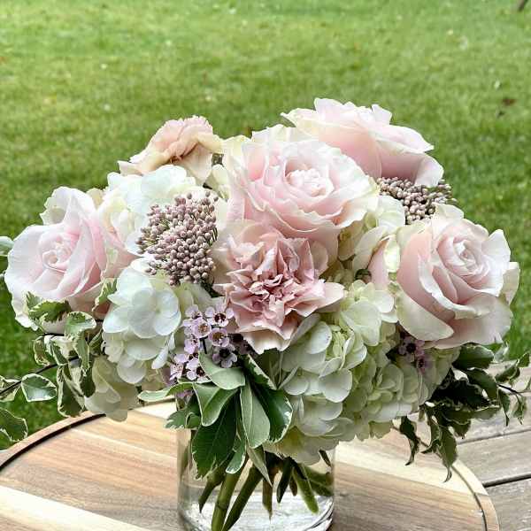 Blush roses and pale hydrangeas arranged in a clear glass vase
