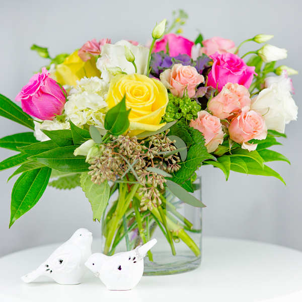 Mixed bouquet of roses and hydrangeas in a glass vase with two white bird figurines