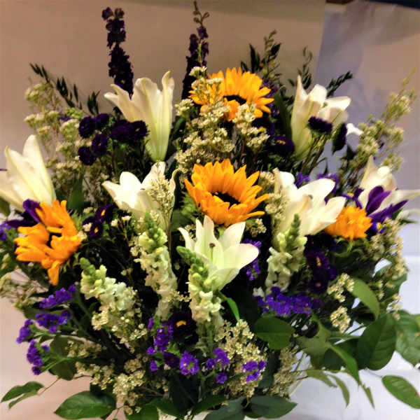 Bouquet of white lilies, sunflowers, and purple flowers in a white vase