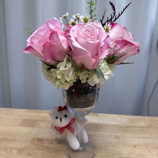 Pink roses and white hydrangeas in a wine glass with a small teddy bear