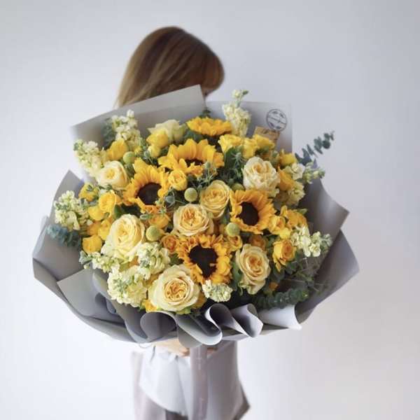 Bouquet of yellow sunflowers and cream roses wrapped in gray paper