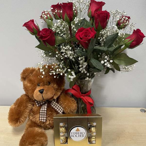 Red roses in a glass vase with a teddy bear and chocolate box