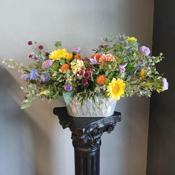 Mixed bouquet in a decorative metal container with yellow, purple, and orange flowers