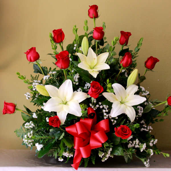 Red roses and white lilies in a low arrangement with a red ribbon bow