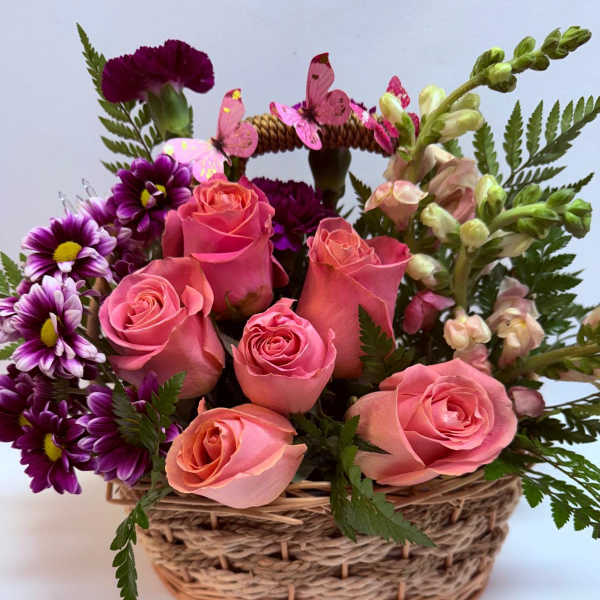 Pink roses and purple daisies in a woven basket with butterfly picks