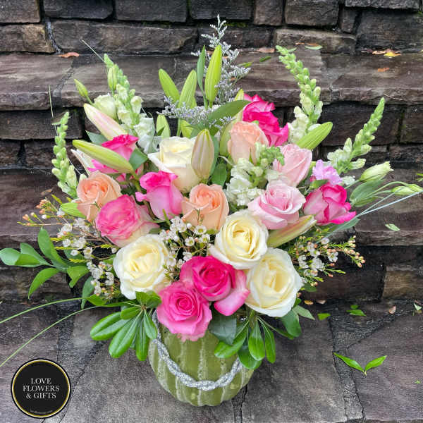Mixed bouquet of pink, peach, and cream roses with lilies and snapdragons in a green vase